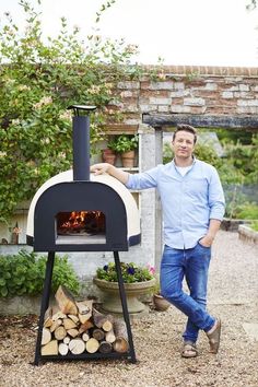 a man standing in front of an outdoor pizza oven with logs and potted plants