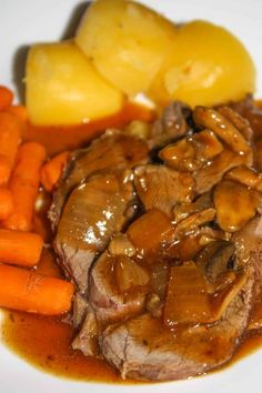 a white plate topped with meat, potatoes and gravy next to carrots