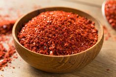 a wooden bowl filled with red spices on top of a table