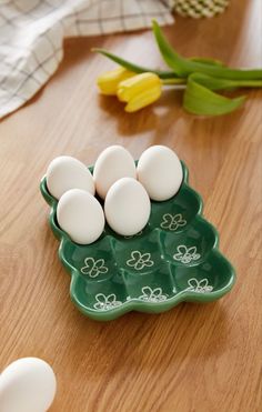 four eggs in a green tray on a wooden table next to tulips and flowers