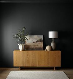 a living room with black walls and white rugs on the floor, two vases sitting on a wooden sideboard