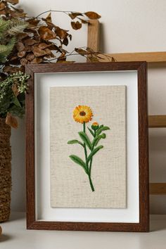 a yellow flower is in a frame next to a potted plant on a shelf