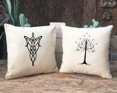 two pillows with designs on them sitting on a table next to cactuses and cacti