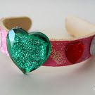 a pink and green bracelet with a heart on the front, sitting on a white surface