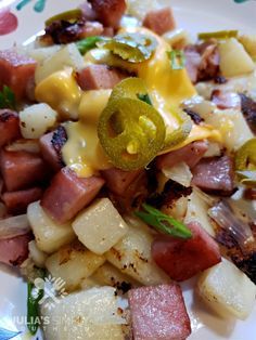 a white plate topped with potatoes and ham covered in cheese on top of green onions