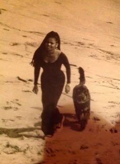 a woman walking her dog on the beach in the sand with another person behind her