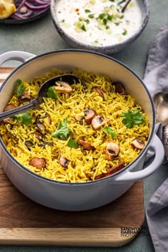 a pot filled with rice and mushrooms on top of a wooden cutting board next to other dishes