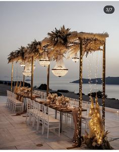 an outdoor dining area with white chairs and lights hanging from the ceiling, surrounded by palm trees