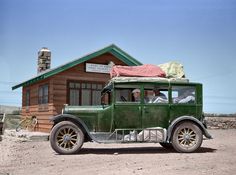 an old green truck is parked in front of a small building with a red tarp on top