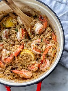 a pot filled with shrimp and rice on top of a white countertop next to a wooden spoon