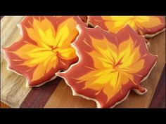 three decorated cookies with orange and yellow leaves on them sitting on a wooden table next to each other