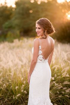 a woman in a wedding dress standing in tall grass with the sun setting behind her