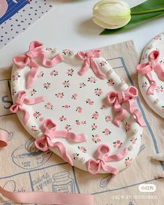 two decorated cookies sitting on top of a table next to pink ribbons and tulips