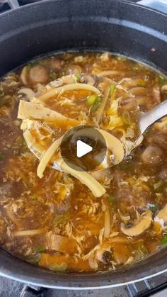 a ladle full of soup with noodles and mushrooms in it, being stirred by a spoon