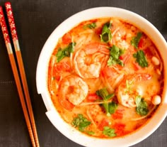 a bowl of shrimp soup with chopsticks next to it on a black surface