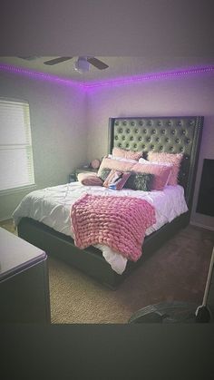 a bedroom with a large bed and purple lights on the ceiling, along with a window