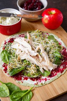 an uncooked pizza sitting on top of a wooden cutting board next to a bowl of cranberry sauce