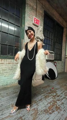 a woman in a black dress and white fur stoler posing for the camera with an exit sign behind her