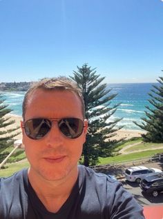 a man wearing sunglasses is taking a selfie in front of the ocean and beach