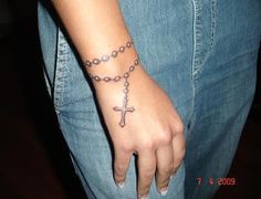 a person with a cross tattoo on their wrist holding a rosary bracelet and wearing blue jeans