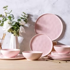 pink dinnerware set on wooden table with flowers in vase