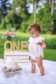 a baby girl standing in front of a cake