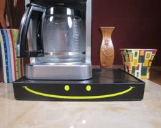 a coffee maker with a smile drawn on it's face sitting on a counter