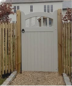 a white house behind a wooden fence with a dog in the gate and bushes around it