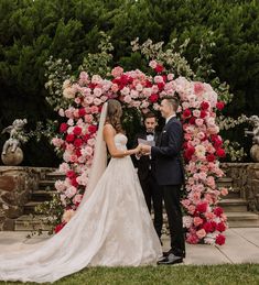 a bride and groom standing in front of a floral arch