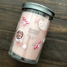 a pink candle with candy canes and candies in it on a wooden table