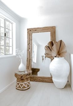 a white vase sitting on top of a wooden table next to a mirror in a room