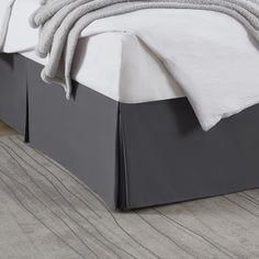 a bed with white sheets and gray bedspread on it's headboard