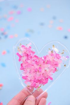 a person holding a heart shaped object with confetti on it's side