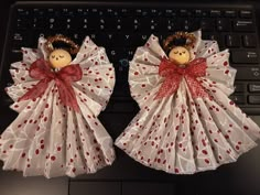 two cloth angel figurines sitting on top of a laptop keyboard, with red bows and polka dots