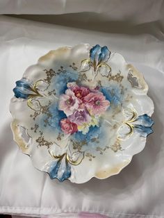 a plate with flowers on it sitting on a white cloth covered tablecloth next to a pink and blue flower