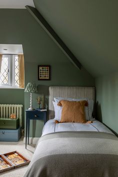 a bed sitting under a window in a bedroom next to a dresser and lamp on top of a wooden table