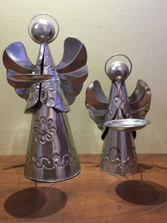 two metal angel figurines sitting on top of a wooden table