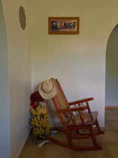 a rocking chair with a hat on it next to a bunch of bananas and a painting