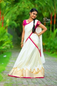 a woman in a white and pink sari standing on a brick path with trees behind her