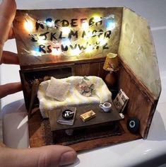 someone is holding up a dollhouse made to look like a bed with lights on it