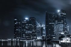 the city skyline is lit up at night with lights reflecting in the water and dark clouds