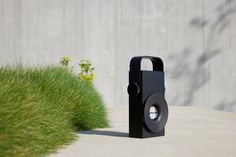 a black object sitting on top of a cement ground next to green grass and bushes