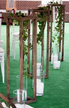 an outdoor ceremony set up with white chairs and greenery on the aisle, along with candles in glass vases