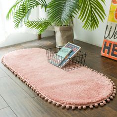 a pink rug with pom - poms on the floor in front of a potted plant