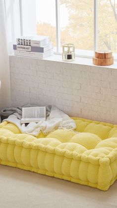 a large yellow bed sitting in front of a window next to a white brick wall