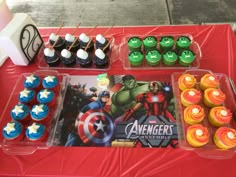 a table topped with cupcakes and cakes covered in fondant captain america decorations