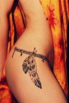 a woman's stomach with a feather and arrow tattoo on the side of her body