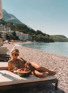 a woman sitting on a beach with a bowl of food