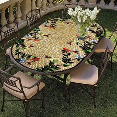 a mosaic table and chairs on the grass with flowers in vases at the end