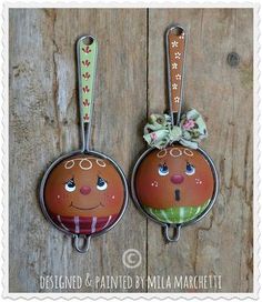 two metal ornaments with faces are hanging on a wooden surface, one has a bow and the other has a flower